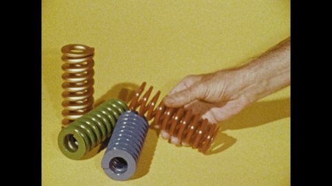 1970s: Four large springs and a hand holds one. Assortment of colored metal Raymond Die springs.