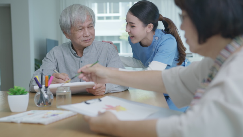 Attractive young senior asian citizen couple sit at home watercolor painting artwork on desk table with nurse feeling happy in mental health therapy or asia older people quarantine activity lifestyle. | Shutterstock HD Video #1065713926