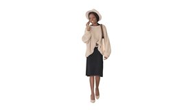 Frustrated african american woman in knitted sweater and white hat talking on her phone on white background.