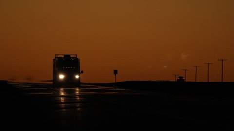 Pickup truck pulling large enclosed trailer. Dusk in Saskatchewan.
Dusk with orange sky. Pickup truck with trailer approaches and passes. HWY 1 TransCanada highway in Saskatchewan, Canada. 

