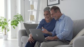 Happy senior couple talking looking at laptop making online video call. Middle aged old grandparents enjoying virtual distance meeting online chat looking at computer sitting on couch at home. - Powered by Shutterstock - Get 15% off with code: PIKWIZARD15