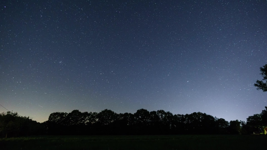 moving night sky over rural landscape with field in front of trees