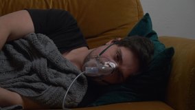 Guy lying on couch at home and breathe with a respirator mask