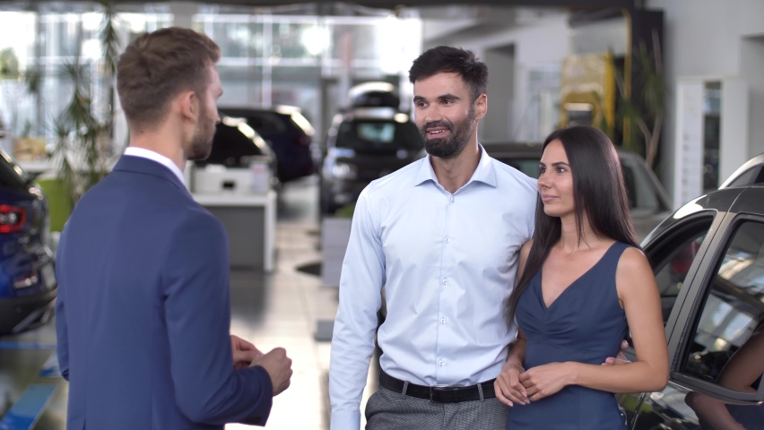 Happy husband and wife getting car keys from auto dealer while buying automobile in dealership. Smiling couple of buyers taking key to purchased from salesman | Shutterstock HD Video #1065724456