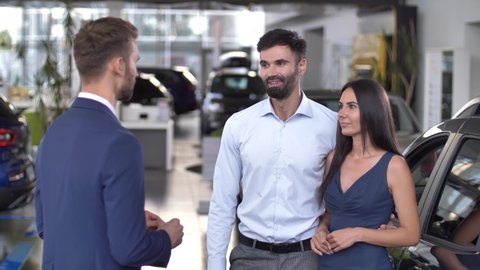 Happy husband and wife getting car keys from auto dealer while buying automobile in dealership. Smiling couple of buyers taking key to purchased from salesman