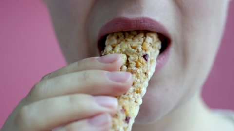 Girl eating protein bar on a pink background close-up