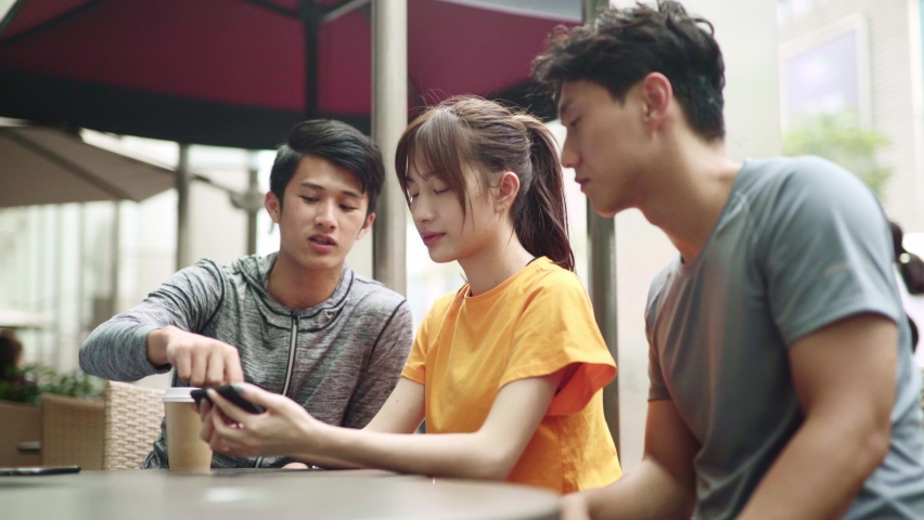 three young asian adult looking at cellphone talking oudoors