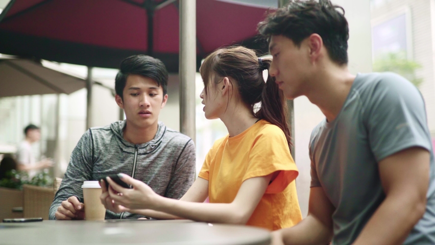 three young asian adult looking at cellphone talking oudoors
