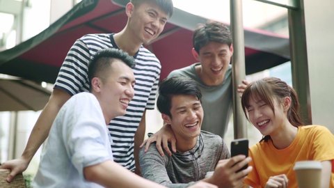 group of young asian adults looking at cellphone together happy and smiling