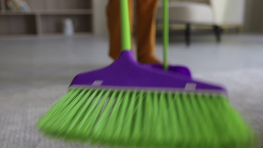 Closeup view of african American boy cleaning floor with brush while standing in home room. Handsome child cleans soft carpet and holding tools in his hands. Kid loves to do household chores and | Shutterstock HD Video #1065738802