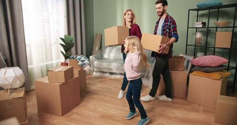 Happy Caucasian family couple moving home into new apartment with adorable little girl daughter discussing redecoration of furniture unpacking boxes and getting settled. Home comfort. Relocating day