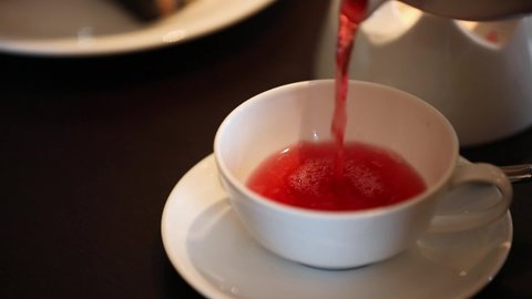 Hand pouring a red tea drink from a teapot to a cup. 