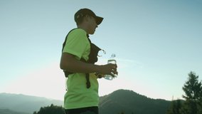Athlete runner refreshes his face and body with the water on the top of the hill with mountain view. Golden sunset light and slow motion video.