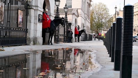 LONDON - NOVEMBER 3, 2020: Mounted trooper of the Household Cavalry and armed Metropolitan Police standing guard at the entrance to Horse Guards Parade. Reflection in puddle on the ground.