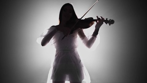 A young attractive women play violin. Violinist in  black studio. Music performance. Musician. Art. Smoke background