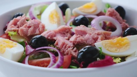 Tuna salad with egg, olives and vegetables in white bowl, white background. Diet food concept.