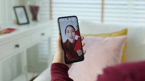 Point of view selfie videocall shot of attractive beautiful young asian lady in red chinese new year celebration outfit happy smile talk and looking to camera mobile phone wishing for lunar festival.
