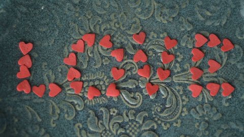 Red scarlet heart figure sugar confetti laid down in shape word love blown away from green plate on green surface. Breaking up end of romantic relationship design concept