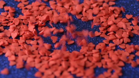 Red scarlet heart shaped sugar confetti piece lies, more fall down cover scatter blue shiny surface slow motion. Romantic love, affection or Saint Valentine's Day preparation design concept