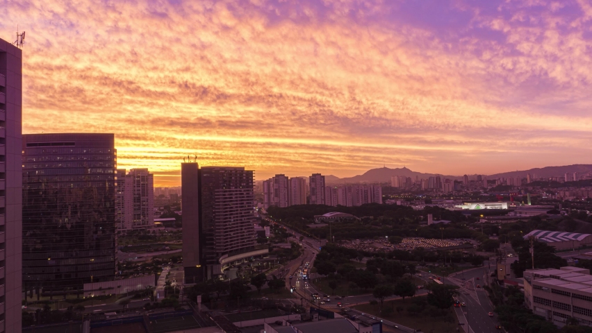 Purple Sunset time-lapse during twilight in urban landscape with cars traffic in a rush moving on avenue and among buildings in São Paulo City Brasil with Jaragua Peak on the background