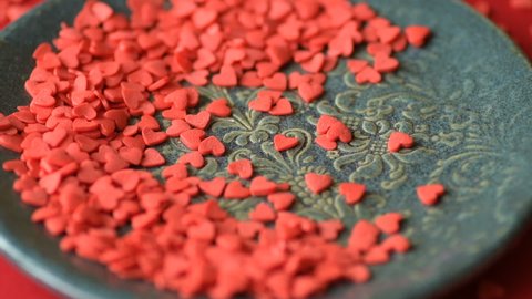 Red scarlet heart shaped sugar confetti crumbling and falling down on green plate on red tablecloth cloth. Romantic love, affection or Saint Valentine's Day preparation design concept
