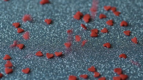 Red scarlet heart shaped sugar confetti piece lies, more fall down cover scatter light blue shiny surface slow motion. Romantic love, affection or Saint Valentine's Day preparation design concept