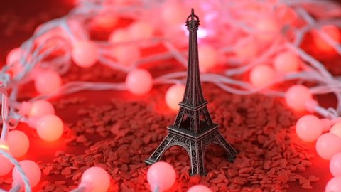 Eiffel tower statuette blurred lights garland background red scarlet heart shaped sugar confetti fall down scatter in slow motion. France, romantic love, Valentine's Day preparation design concept