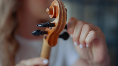 Teenage girl hands tuning violin. Young woman checking pegs of violin. Closeup female violinist tuning musical instrument. Lady holding string instrument in hands