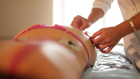 A beauty therapist attaches electrodes to the butt for electro myo stimulation therapy.Hardware cosmetology and antiage therapy.