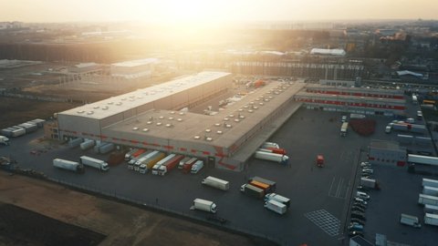 Logistics park with a loading hub. There are many semi-trailers trucks stand at the warehouse ramps for load and unload goods from cargo containers. Aerial all-round view