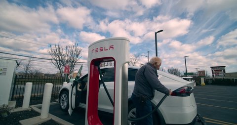 Staten Island, New York  United States - January 17,  2021: Time-laps, Tesla electric car pulls into Supercharger power station. Driver gets out and connects car to charger.
