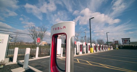 Staten Island, New York  United States - January 17,  2021: Tesla electric car Supercharger power station in strip mall parking lot. Time-lapse of clouds passing overhead.
