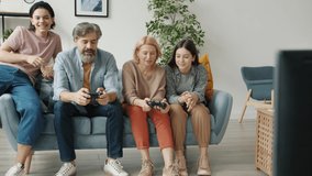 Mother and father are playing video game while kids are cheering eating popcorn then laughing doing high-five indoors in modern apartment