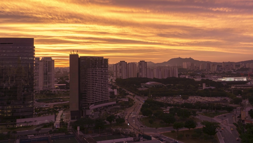 Sunset time-lapse during twilight in urban landscape with cars traffic in a rush moving on avenue and among buildings in São Paulo City Brasil with Jaragua Peak on the background