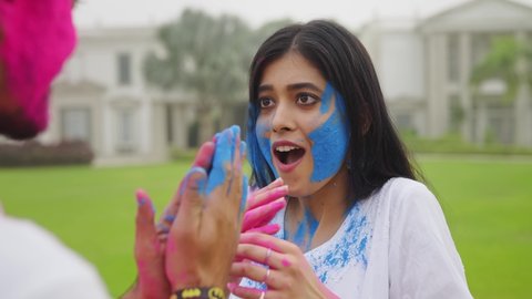 A close view shot of a happy young Indian couple playing with powdered colors near a lawn smearing on each other face. High-speed shot of  attractive friends celebrating Indian Hindu festival Holi
