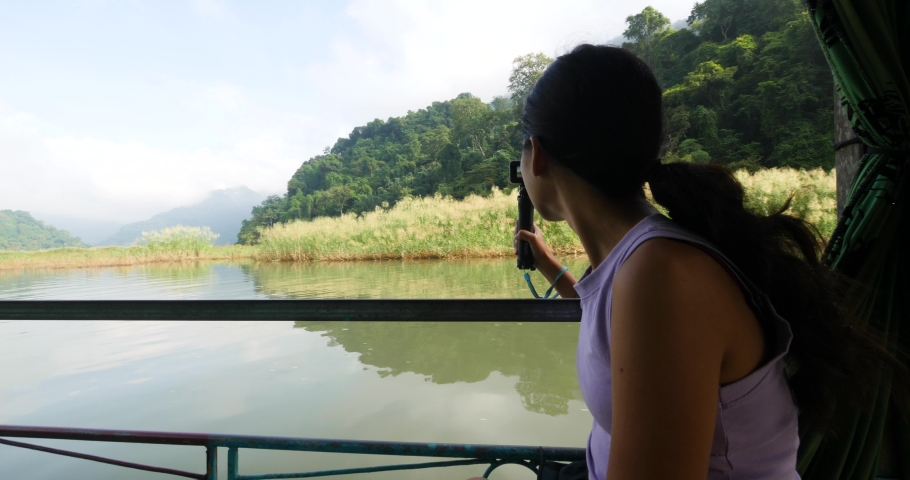 A young Asian woman on the boat in the lake with action camera filming video.