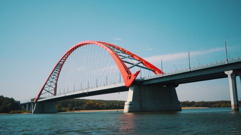 Cars drive across the red arched bridge in Novosibirsk. High modern bridge in Russia.