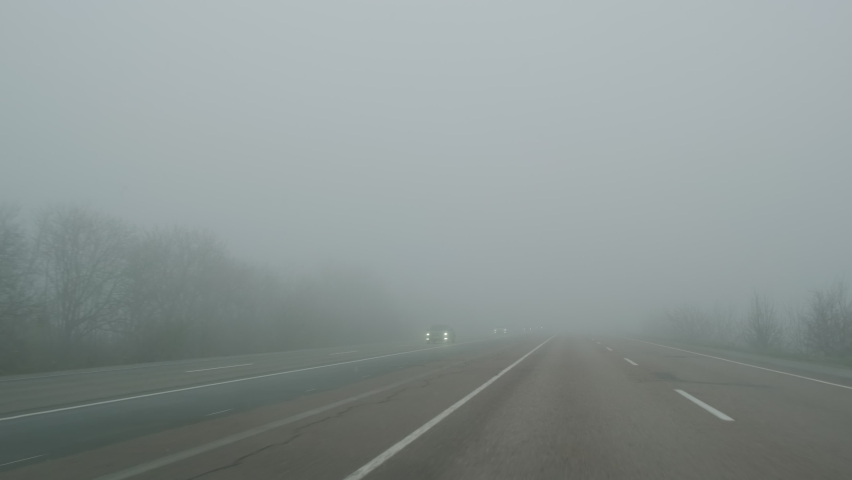 Cars move on foggy road, view through windshield in daytime. Cars pass through fog on road. Poor visibility in mist highway. Dangerous weather for driving. Cars keep distance at haze Royalty-Free Stock Footage #1065801172