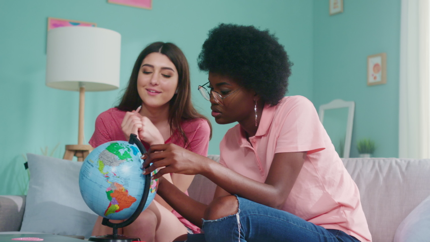 Young women, students are sitting on sofa at home and researching the globe, working on common academic project, enjoy studying, Foreground, Slow motion.