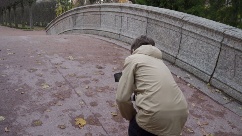 Vlogger boy with mobile phone camera stabilizer recording outdoor video blog in autumn park. Teenager shooting video for travel vlogging. Catherine Park, Tsarskoye Selo, Saint Petersburg, Russia.