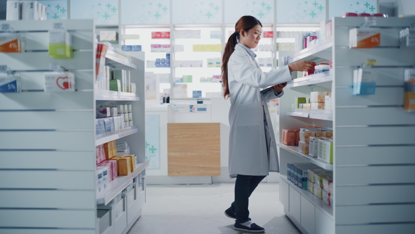 Pharmacy Drugstore: Beautiful Chinese Pharmacist Uses Digital Tablet Computer, Checks Inventory of Medicine, Drugs, Vitamins, Health Care Products on a Shelf. Professional Druggist in Pharma Store Royalty-Free Stock Footage #1065814249
