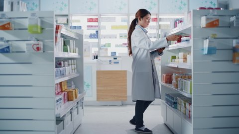 Pharmacy Drugstore: Beautiful Chinese Pharmacist Uses Digital Tablet Computer, Checks Inventory of Medicine, Drugs, Vitamins, Health Care Products on a Shelf. Professional Druggist in Pharma Store