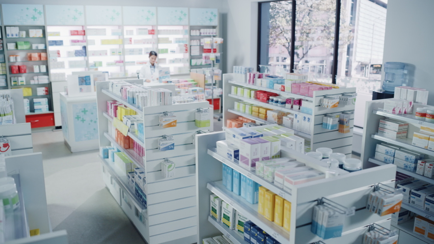 Big Modern Pharmacy Drugstore with Shelves full of Packages Full of Modern Medicine, Drugs, Vitamin Boxes, Pills, Supplements, Health Care Products. Pharmacist Standing at Counter. Establishing Shot Royalty-Free Stock Footage #1065814396
