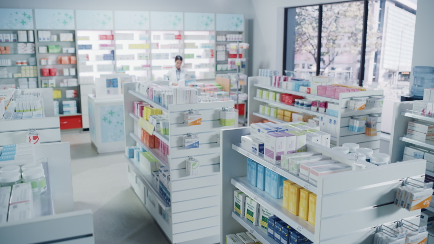 Big Modern Pharmacy Drugstore with Shelves full of Packages Full of Modern Medicine, Drugs, Vitamin Boxes, Pills, Supplements, Health Care Products. Pharmacist Standing at Counter. Establishing Shot | Shutterstock HD Video #1065814399