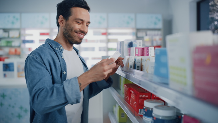 Pharmacy Drugstore: Portrait of Handsome Latin Man Choosing to Buy Medicine Browsing through the Shelf, Successfully finds what he Needs, Smiles Happily. Modern Pharma Store Health Care Products