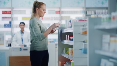 Pharmacy Drugstore: Beautiful Young Woman Chooses to Buy Medicine, Drugs, Vitamins, Searches Shelves for the Best Choice. Modern Pharma Store Shelves with Health Care, Beauty Products