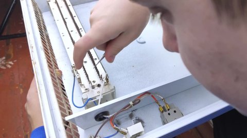 An electrical repairman repairs a convector. A close-up of an open heater and its interior. Technical assistance concept