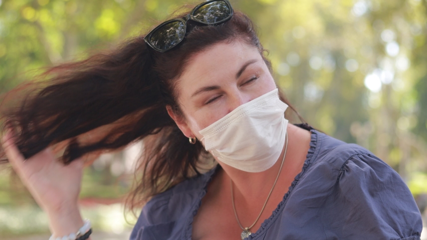 A woman in a protective mask walks in the park on a sunny summer day.	
