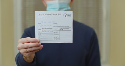 Lviv, Ukraine - January 14, 2021: Man in madical mask is holding a vaccination record card. Passport of immunity to the coronavirus in the hands of a male. Health passport as proof of recovery from