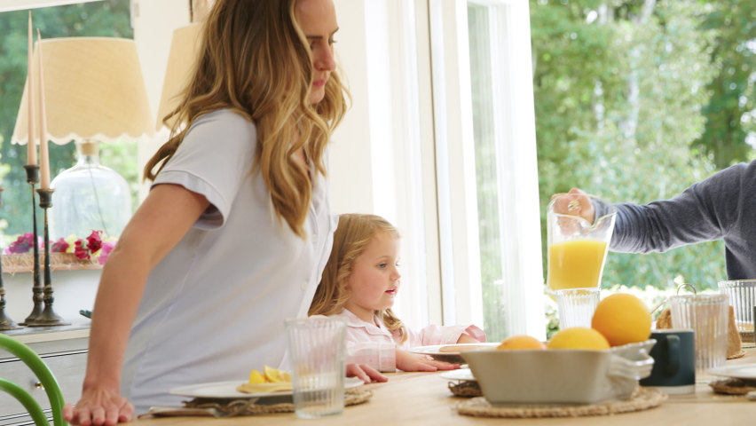 Father pouring orange juice as family wearing pyjamas sit around table enjoying pancake breakfast together - shot in slow motion Royalty-Free Stock Footage #1065817507